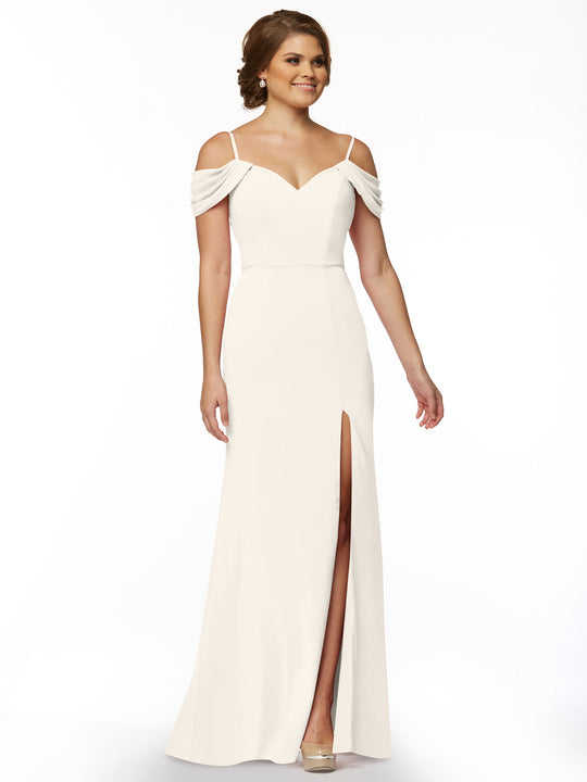 A woman models Avery Austin’s 83029: a long, off-the-shoulder dress with draped sleeves and a thigh-high slit, posed against a plain white background.