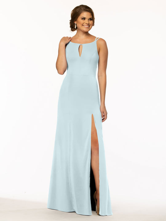 A woman in the Avery Austin 83030 sheath dress in sky blue, featuring a sleeveless design, pockets, a front keyhole cutout, and a high side slit, stands against a white background, smiling and touching her hair.