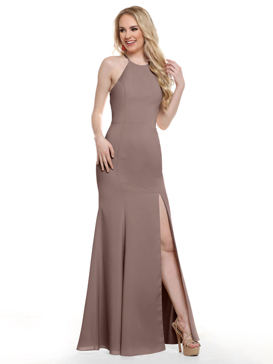 A woman in the Avery Austin 83031, a sleeveless, floor-length taupe fitted dress with a high slit, smiles against a plain white background. She has long, wavy blonde hair and wears nude high-heeled shoes.