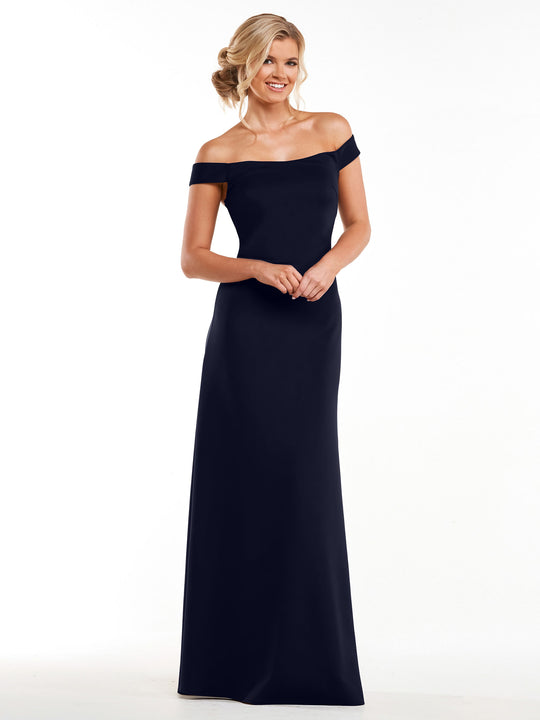 A woman in Avery Austin's navy sheath dress (style 83055) stands against a white background, her hair styled in soft, pinned-up waves. She smiles and gazes slightly to the side.