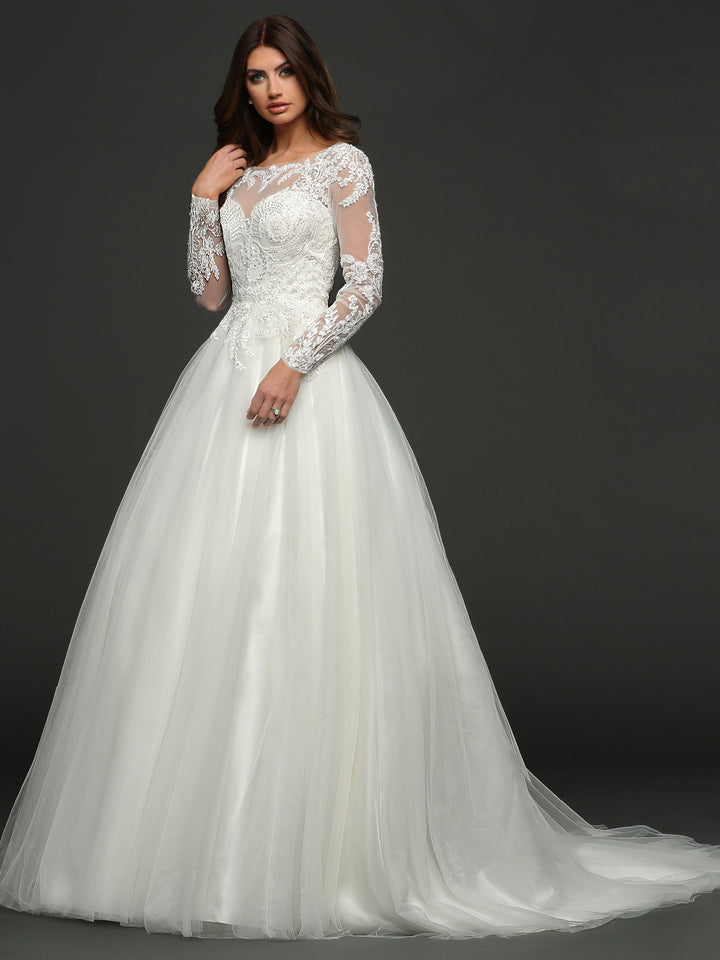 A woman in the “Victoria” ivory wedding dress by Avery Austin, featuring long sleeves, lace details, a full tulle skirt, and a ball gown silhouette, stands against a dark background.