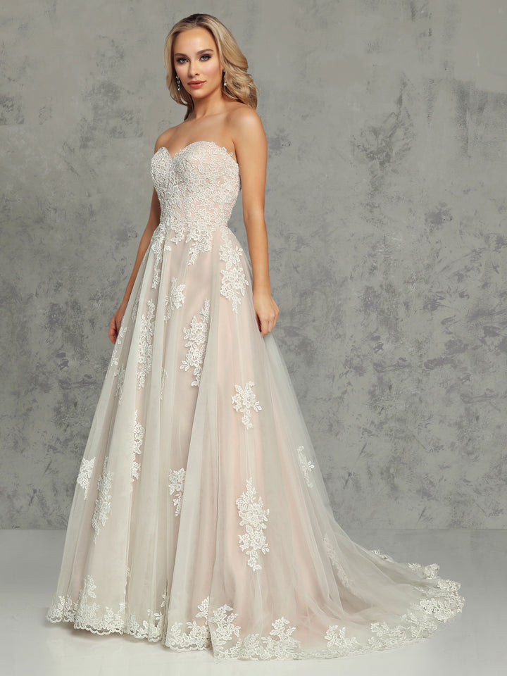 A woman wears the Avery Austin TH-Addison wedding dress in Ivory/Blush, featuring a strapless sweetheart neckline, lace appliques, and a fitted bodice, standing before a gray textured background.