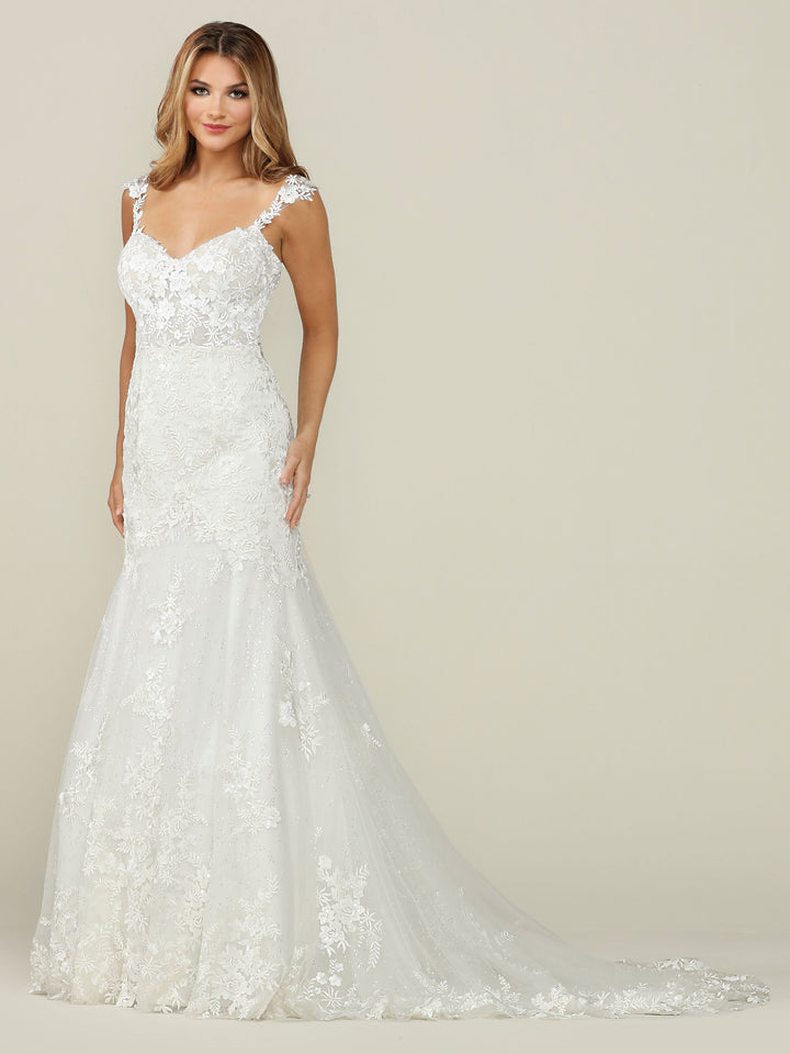 A woman models Avery Austin’s TH-Nevaeh wedding dress in Ivory/Ivory, featuring a fitted bodice, cap sleeves, elegant lace, and a flowing train in a graceful fit-and-flare silhouette against a simple light background.