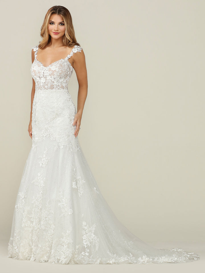 A woman wears the Avery Austin "Nevaeh" wedding dress in Ivory/Nude, featuring a floor-length lace design with a fitted bodice, cap sleeves, and a long train, standing against a plain light background.