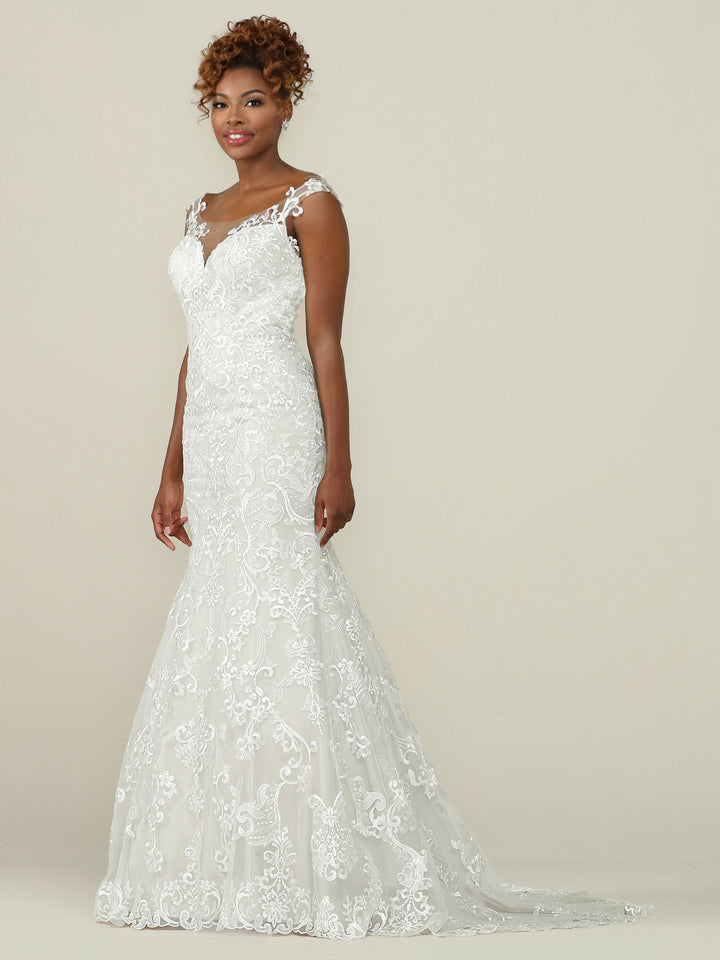 A woman smiles gently at the camera, wearing the Avery Austin TH-Eliana fit-and-flare lace wedding dress in Ivory/Ivory, featuring a sleeveless fitted bodice, floral appliqué, and a slight train, against a plain light background.
