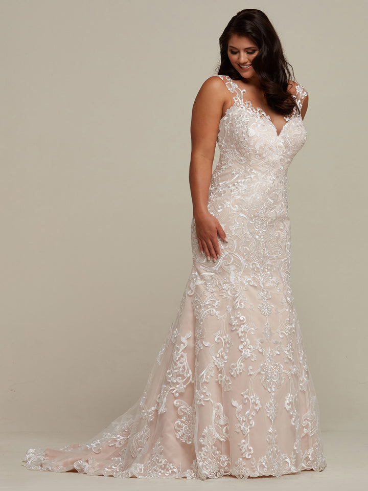 A woman stands against a plain light background, smiling and looking down in the Eliana sleeveless lace fit-and-flare wedding dress by Avery Austin.