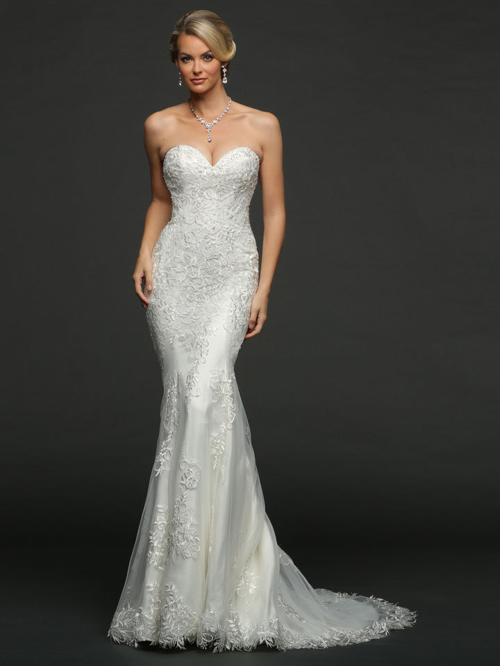 A woman poses elegantly in the Isla wedding dress by Avery Austin, featuring ivory botanical lace appliques, a strapless sweetheart neckline, and a long train against a dark background.