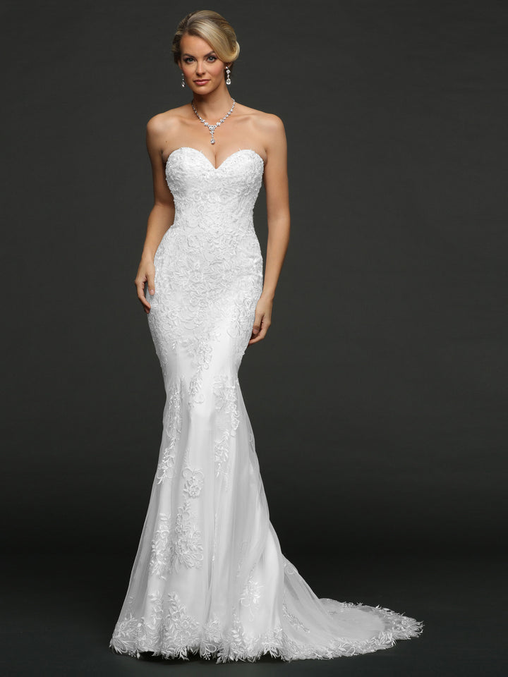 A woman wears the Isla wedding dress by Avery Austin in white, featuring a strapless design with botanical lace appliques, a sweetheart neckline, and subtle train. She pairs it with drop earrings and a necklace against a dark background.