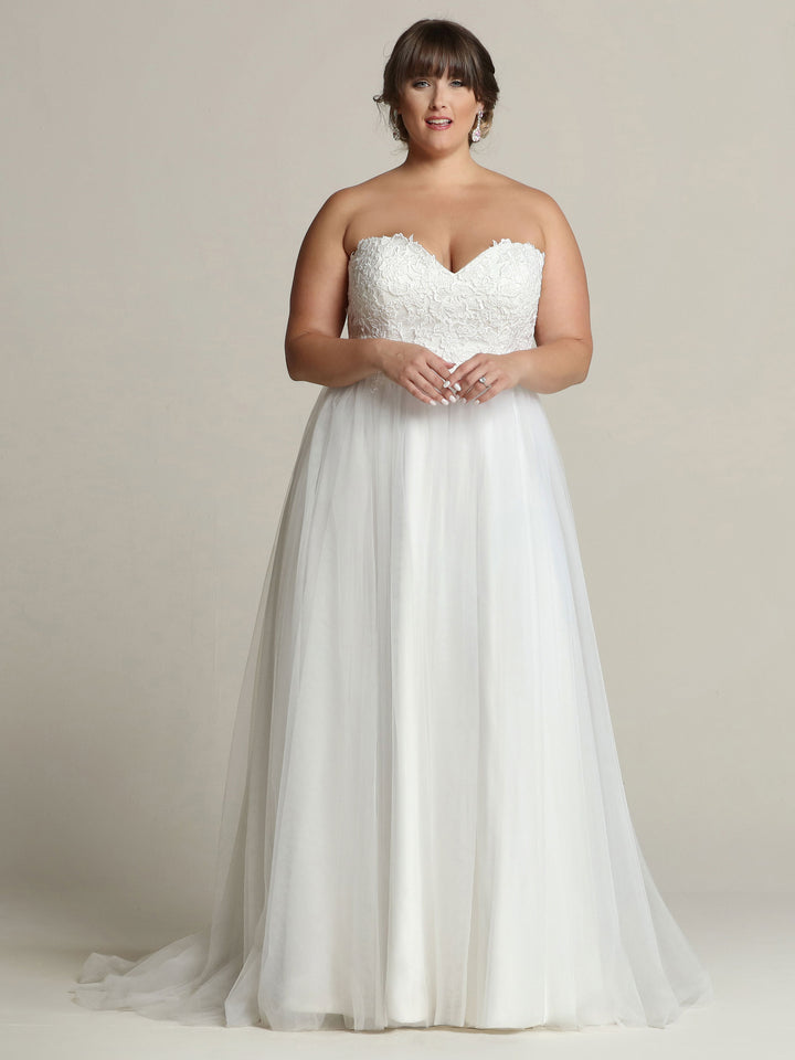 A woman models the Avery Austin TH-Hadley, an ivory strapless A-line wedding dress with a fitted lace bodice and flowing tulle skirt, against a neutral background.
