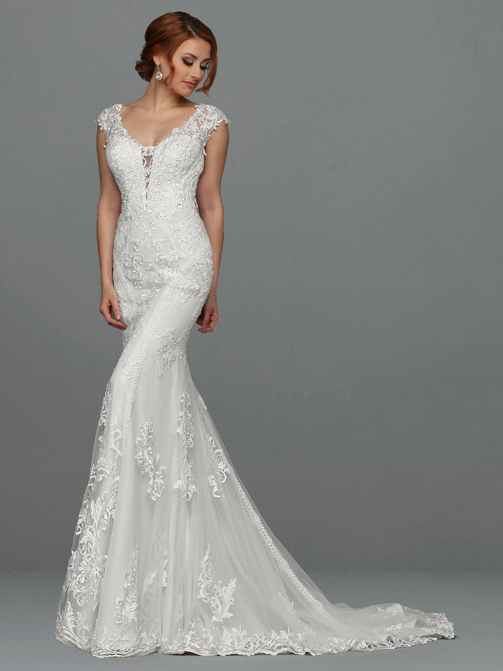 A woman stands against a plain gray background wearing "Faith," an elegant, fitted white lace fit-and-flare wedding dress with cap sleeves and a long, flowing train by Avery Austin.