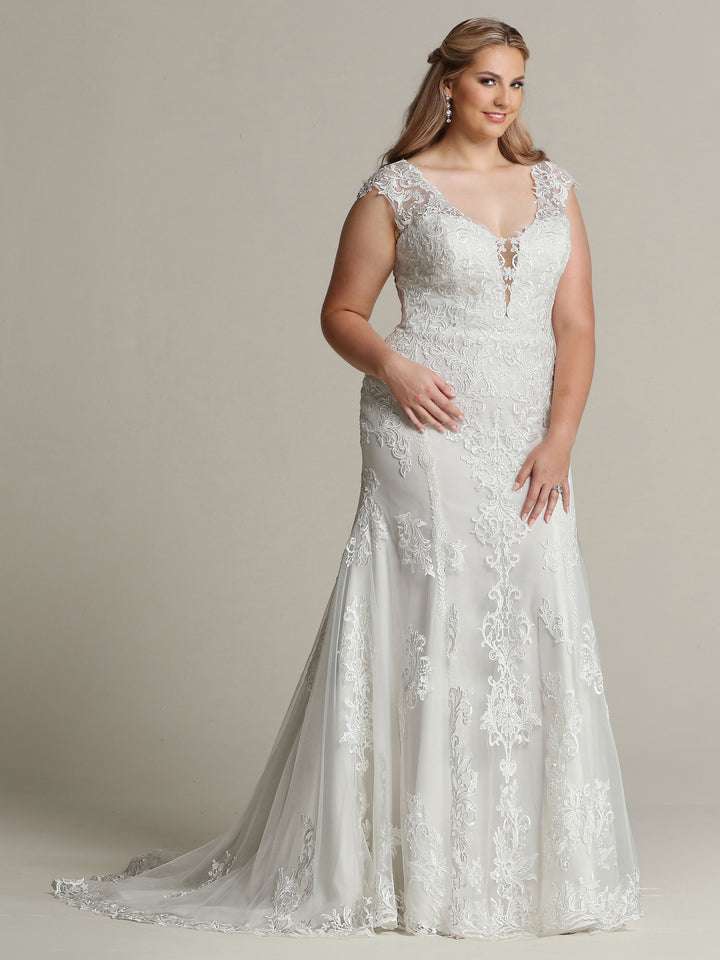 A woman stands against a plain background, smiling softly in the "Faith - Tried On Sample" sleeveless lace wedding dress by Avery Austin in Ivory/Ivory, featuring a fitted bodice and flared, floor-length skirt.