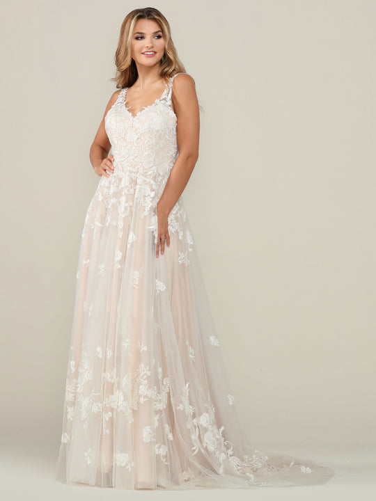 A woman smiles in the Iris wedding dress by Avery Austin, an ivory/champagne lace a-line gown with a v-neck, sheer overlay, floral appliqués, sleeveless design, and flowing skirt. The background is plain and light-colored.