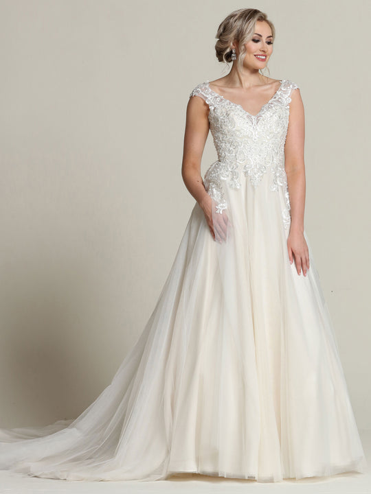 A woman in the Avery Austin Sara - Tried On Sample wedding dress, featuring ivory/sand lace with cap sleeves and a flowing tulle skirt, stands before a plain background, smiling to the side. This elegant A-line gown radiates timeless charm.