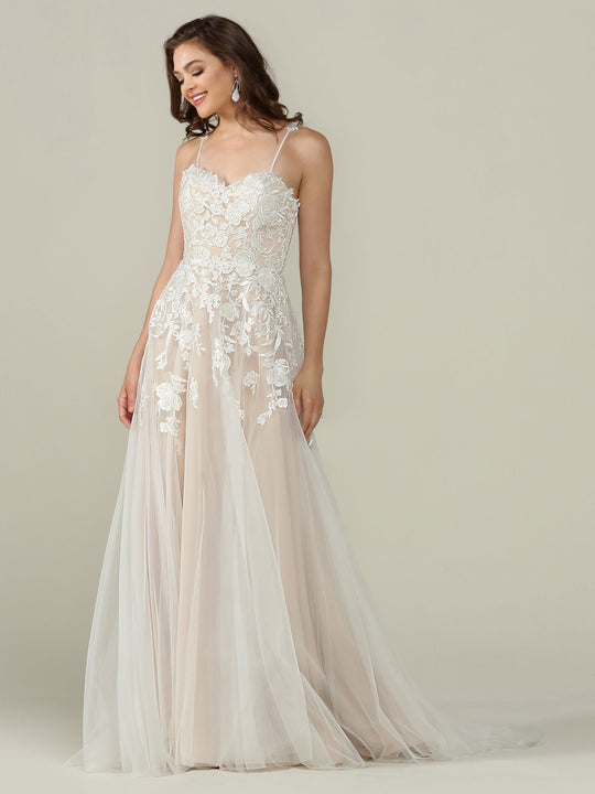 A woman in the Avery Austin TH-Esther wedding dress—sleeveless, floor-length with ivory/champagne lace, floral embroidery, and a tulle skirt—stands against a plain light background, smiling and looking to the side.