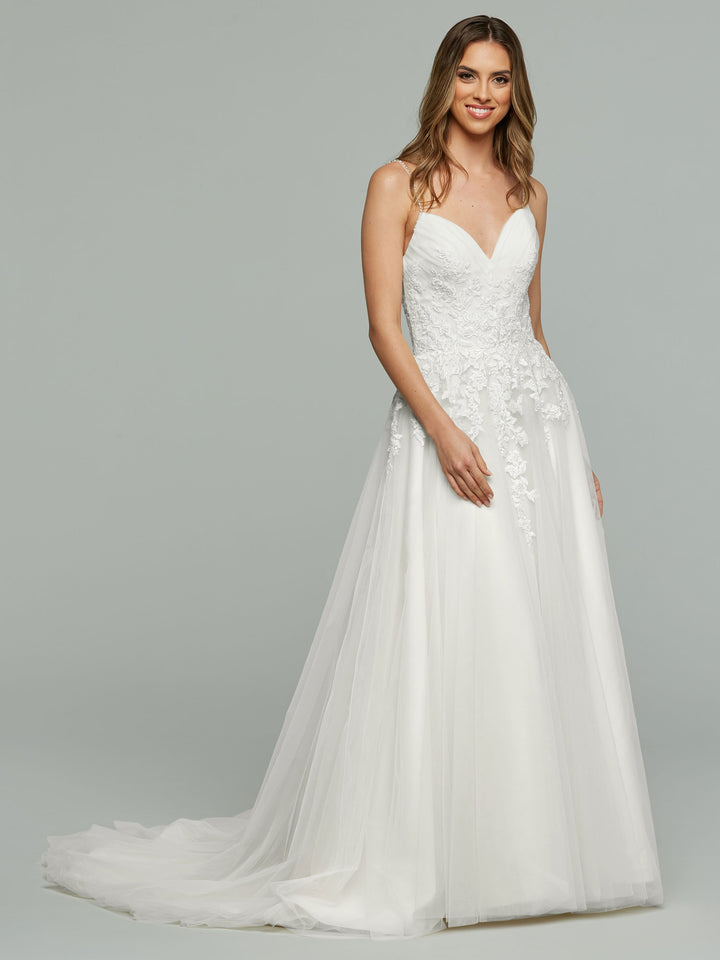 A woman stands against a gray background, smiling in the Vanessa - Tried On Sample by averyaustin—a white, floor-length A-line wedding dress with a fitted bodice, floral lace appliques, and a flowing tulle skirt.