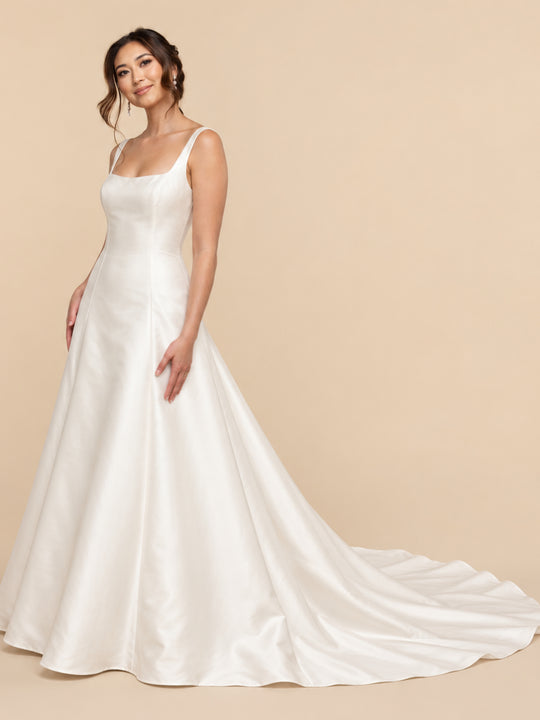 A woman wears the Amelie by averyaustin, a white satin A-line wedding dress with a square neckline and a long train.
