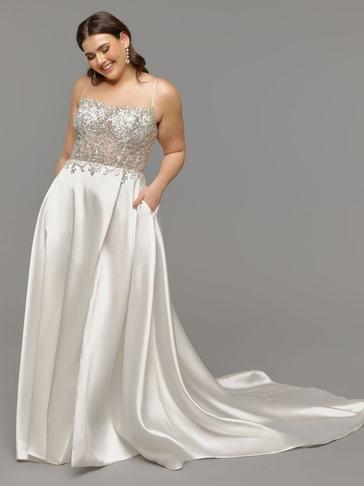 A smiling woman models the Avery Austin TH-Mariam, an ivory wedding dress featuring a beaded lace and sheer bodice, spaghetti straps, floor-length satin skirt with pockets, and a long train, against a plain gray background.