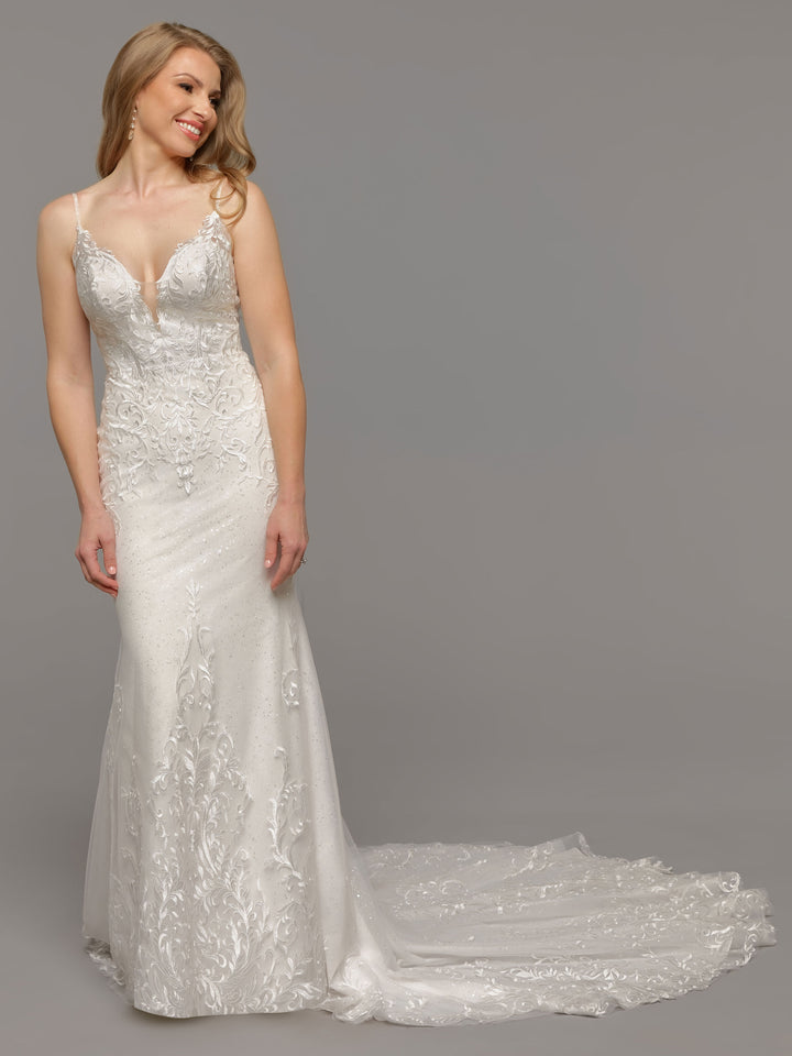 A woman smiles and looks left, wearing the averyaustin "Malia" wedding dress in Ivory/Sand—a white, sleeveless lace gown with a long train and delicate tulle details—posed against a gray background.