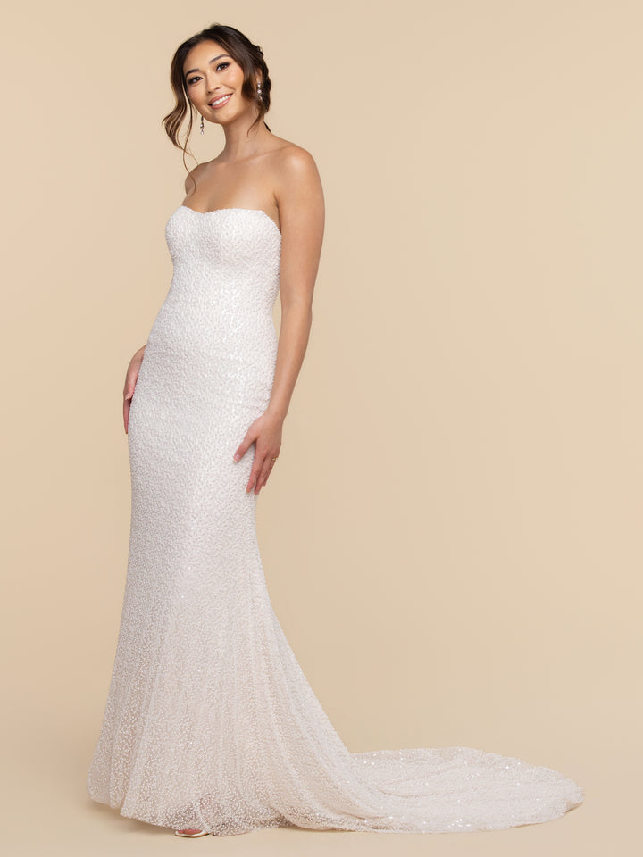 A woman wearing the Alessia floor-length, strapless gown with a scoop neckline, covered in white sequins with a small train.