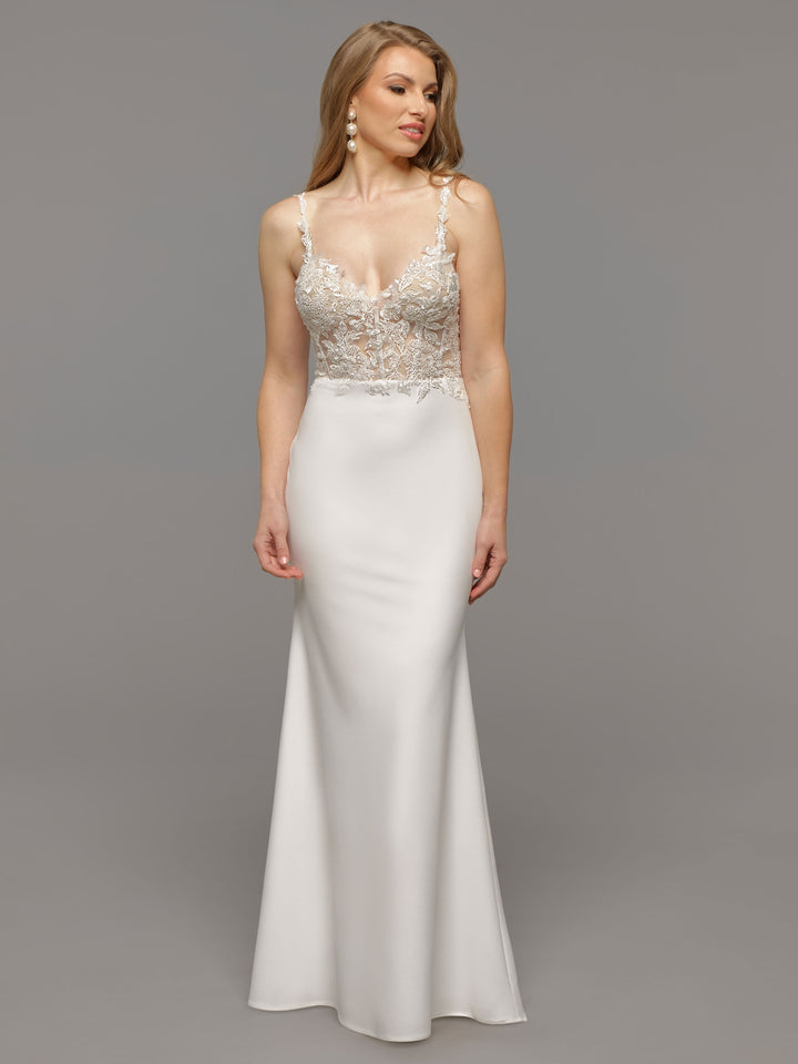 A woman models the Avery Austin TH-June wedding dress: a floor-length, open-back white gown with a fitted satin skirt and sheer, beaded lace bodice. She has long, wavy hair and poses against a plain gray background.