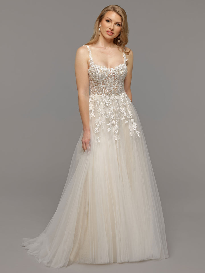 A woman models the Coco by averyaustin—a floor-length, sleeveless white lace wedding dress with a sheer embroidered bodice and floral appliqué—against a plain gray background.