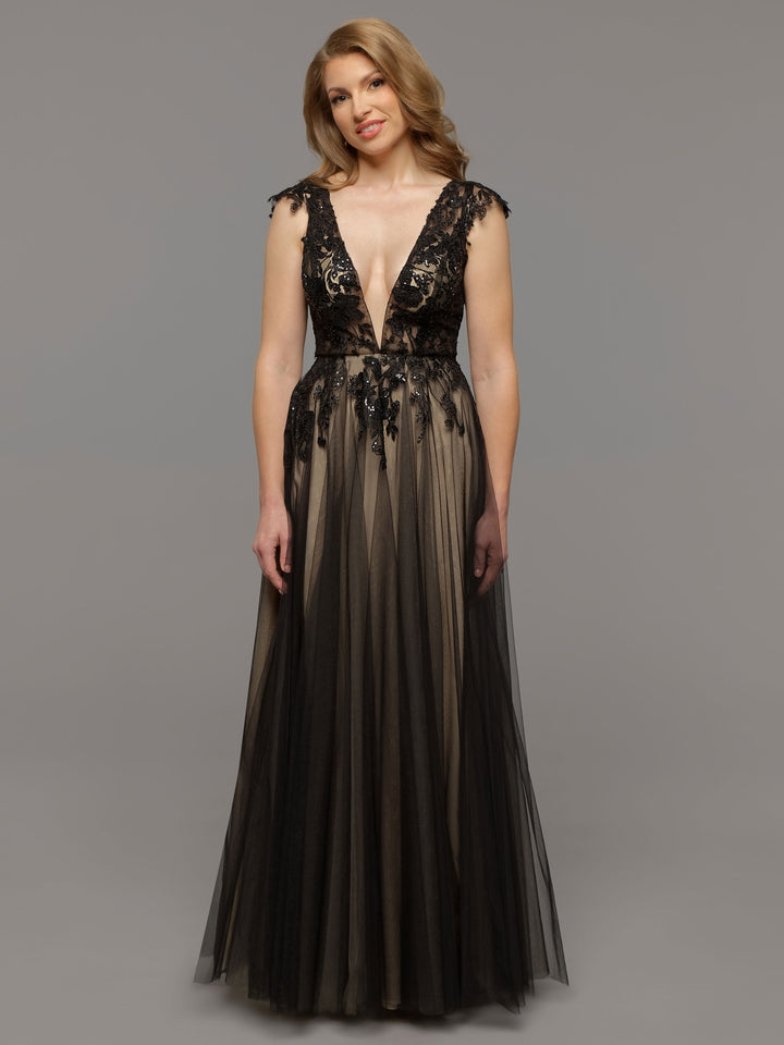 A woman stands against a plain gray background wearing the Hana floor-length gown by averyaustin in Black/Nude, featuring a deep V neckline, sheer tulle overlay, and floral lace bodice detailing.