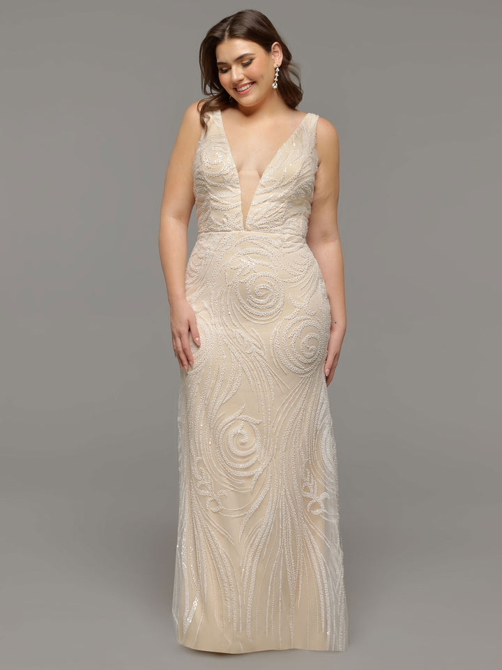 A woman in the Avery Austin TH-Mabel wedding dress—an ivory, sleeveless, floor-length v-neck gown with swirling beadwork—stands smiling against a plain gray background.
