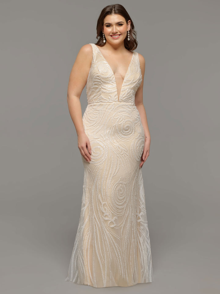 A woman wearing the Avery Austin TH-Mabel, an ivory/ivory, sleeveless, floor-length beaded lace wedding dress with a deep V-neckline and swirling embellishments, stands against a plain light gray background.