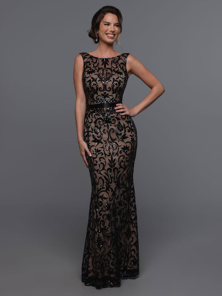 A woman wearing Avery Austin’s TH-80091, a sleeveless floor-length black/nude dress, stands against a gray background, smiling with one hand on her hip.