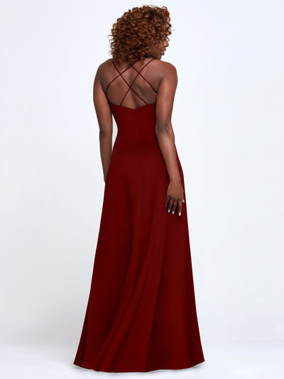 A woman with curly hair models Avery Austin’s 83045, a long dark red A-Line dress with cross back crisscross straps and an open back, posing to showcase the elegant back design against a plain white background.