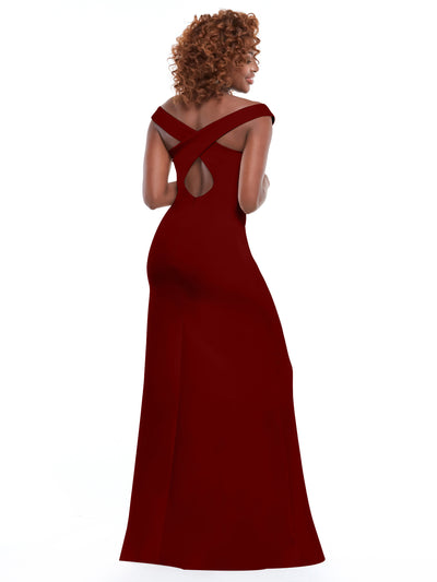 A woman with curly hair models Avery Austin's 83052: a long, elegant off-the-shoulder bridesmaid dress with crisscross straps, a keyhole back, and a thigh-high slit, standing against a plain white background.