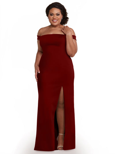 A woman in Avery Austin's 83052 burgundy off-the-shoulder bridesmaid dress with a thigh-high slit smiles against a white background. Her curly hair is swept to one side, and she finishes the look with open-toe heels.
