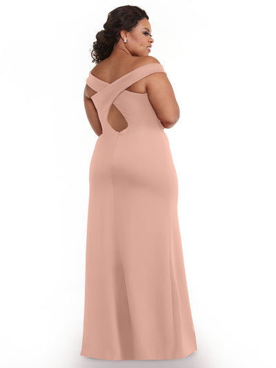 A woman models Avery Austin’s 83052: a blush pink, off-the-shoulder bridesmaid dress featuring a floor-length skirt, crisscross back, and thigh-high side slit, posing with her back turned on a white background.