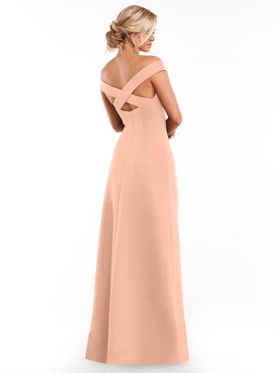 A woman with blonde hair in an updo models Avery Austin style 83055, a long peach sheath dress with a fitted bodice and crisscross back straps, against a white background.