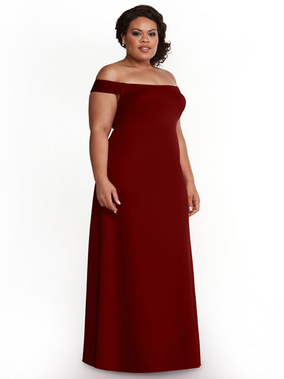 A woman models Avery Austin’s 83055, a floor-length, off-the-shoulder sheath dress in burgundy, standing against a plain white background and facing slightly to the side with a neutral expression.