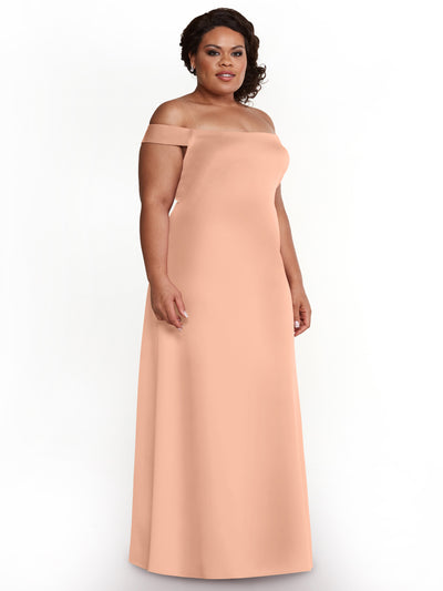 A woman in the Avery Austin 83055 long, off-the-shoulder sheath dress in Petal Pink stands against a white background, looking slightly right and smiling softly.