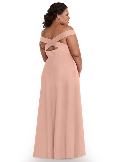 A woman stands with her back to the camera in Avery Austin’s 83055 blush pink, off-the-shoulder, floor-length sheath dress featuring crisscrossed back straps. Her hair falls in soft curls against a plain white background.