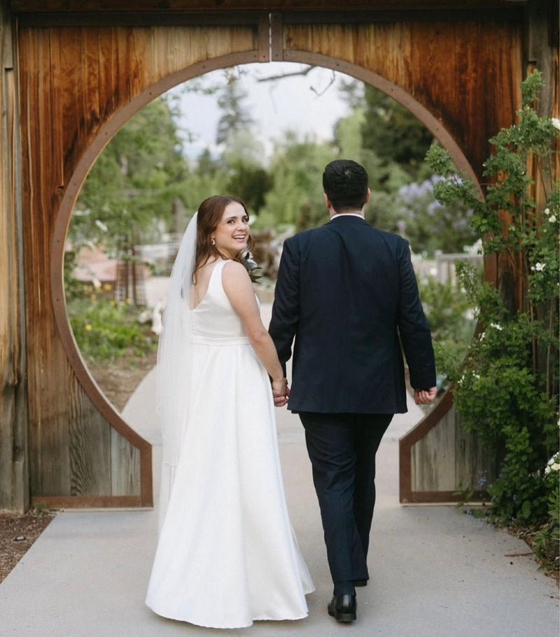 Couple walking under a wooden archway on a wedding day.