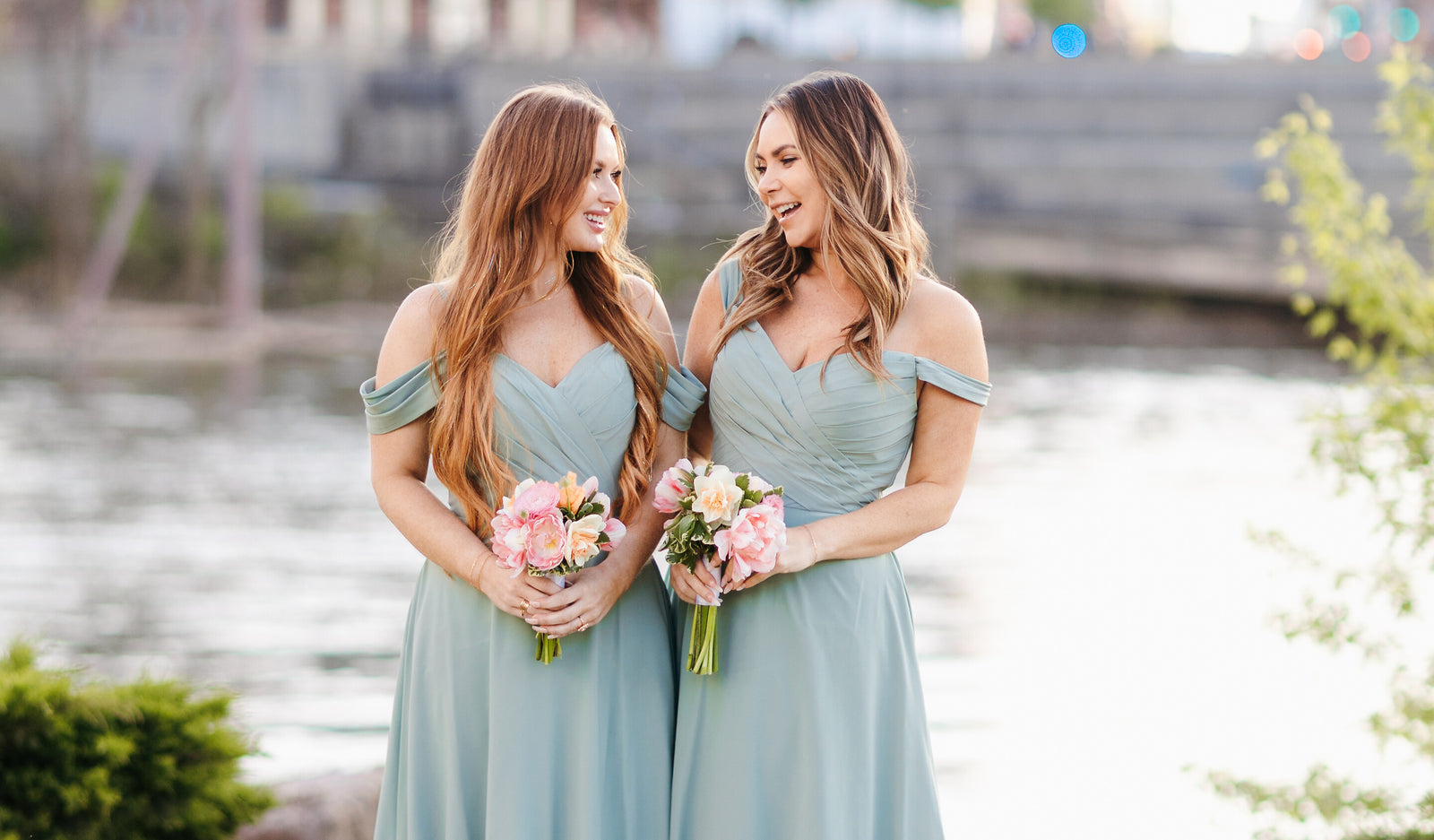 Two bridesmaids in sage dresses by the river at golden hour