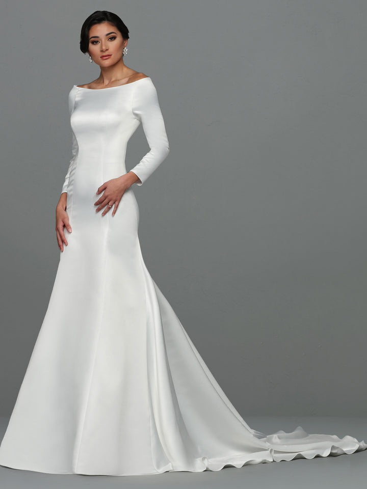 A woman stands against a plain gray background wearing the Avery Austin "Ellie" wedding dress in ivory—a sleek, long-sleeve satin gown with an off-the-shoulder neckline and a flowing train.