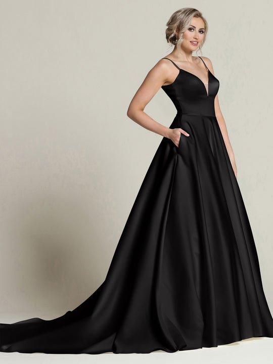 A woman wears the Avery Austin "Melanie" ball gown in black, featuring thin straps, a fitted bodice, pockets, and a full satin skirt. She stands in profile against a plain light background.