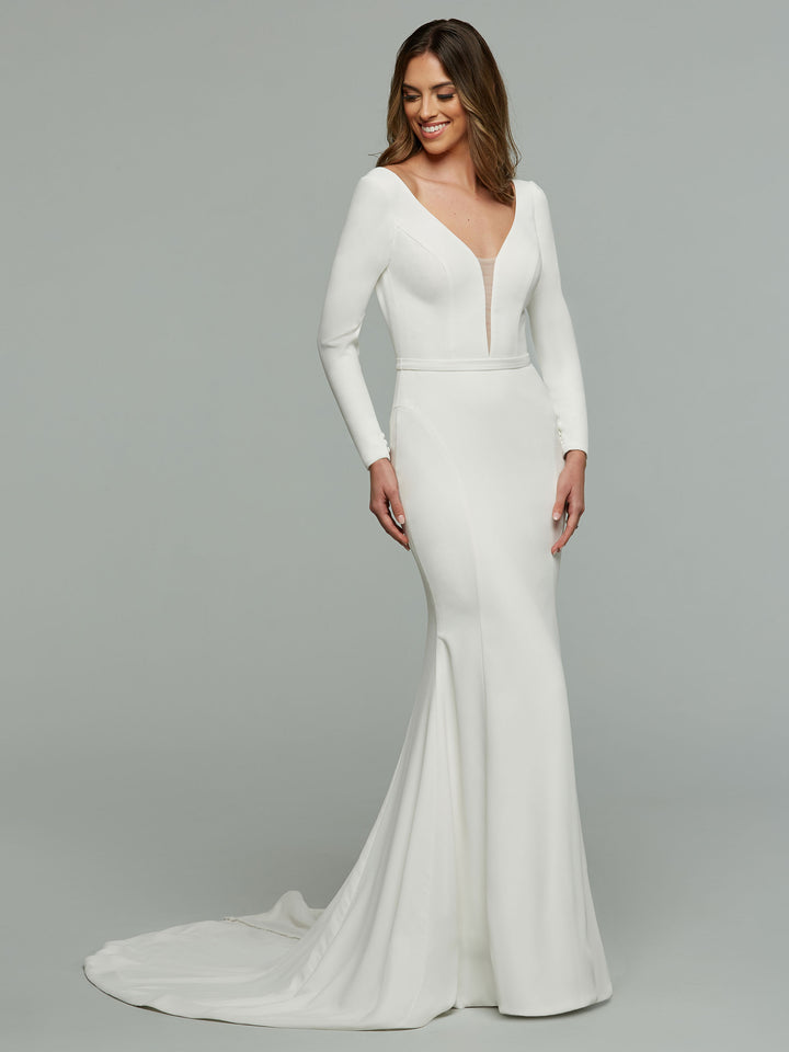 A woman smiles against a plain gray background, wearing the Avery Austin Felicity wedding dress in ivory—a crepe mermaid gown with an illusion plunging v-neckline and short train.
