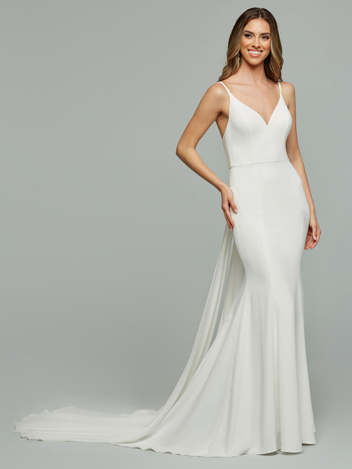 A woman smiles with one hand on her hip, modeling the Harlow by Avery Austin—a sleeveless, fitted ivory crepe mermaid wedding dress with a V-neckline and flowing train—against a plain light gray background.