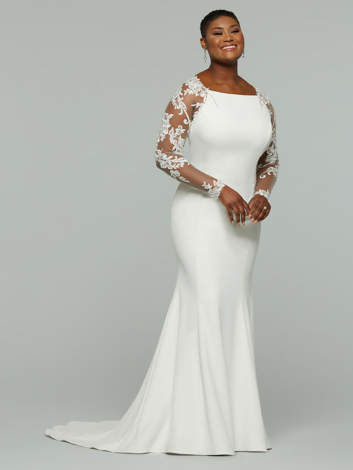 A woman smiles against a plain gray background wearing the Avery Austin Indie dress—an elegant ivory mermaid wedding gown with sheer, floral lace long sleeves and a fitted silhouette.