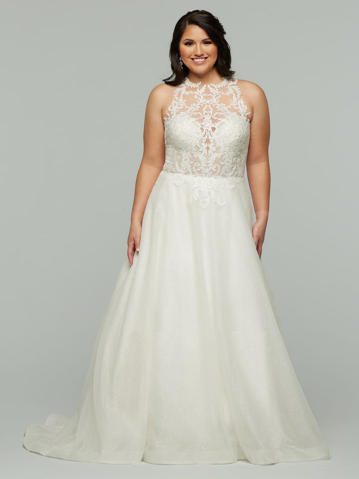 A woman smiles in front of a plain light gray background, wearing the Avery Austin "Jamie" wedding dress in ivory—a beautiful A-line gown with a lace bodice and sheer high neckline.
