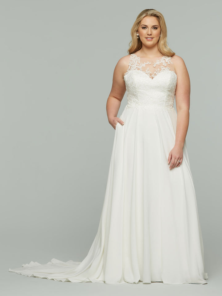 A woman models the Avery Austin Raven dress—a floor-length ivory chiffon A-line gown with a lace bodice, sheer neckline, subtle train, and pockets—standing against a plain gray background.