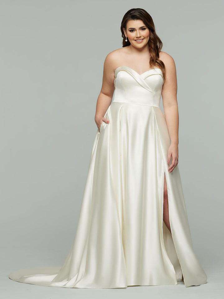 A woman in the Avery Austin TH-Zara wedding dress—strapless, ivory, with a sweetheart neckline, floor-length satin skirt, and thigh-high slit—smiles against a plain gray background.