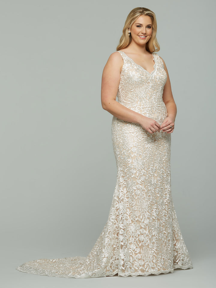 A smiling woman models the Avery Austin "Sloan" dress in Ivory/Nude—a sleeveless, floor-length lace gown with a slight train and elegant mermaid silhouette—set against a plain gray background.