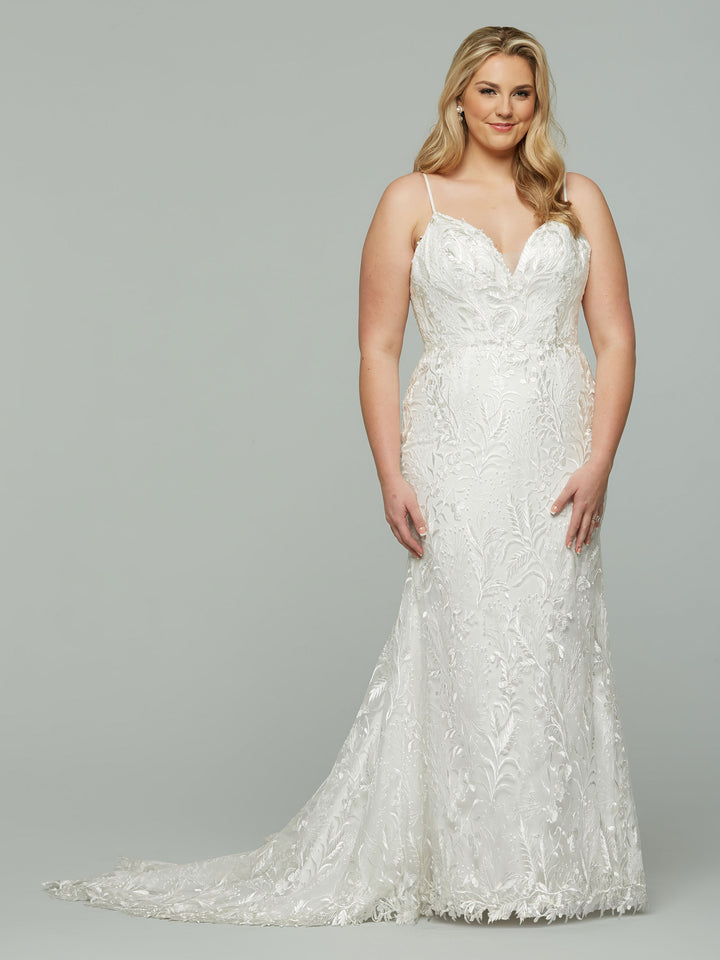 A woman with long blonde hair wears the Avery Austin Celine fitted embroidered lace mermaid wedding dress in Ivory/Nude, featuring thin straps and a subtle train, standing against a plain gray background.