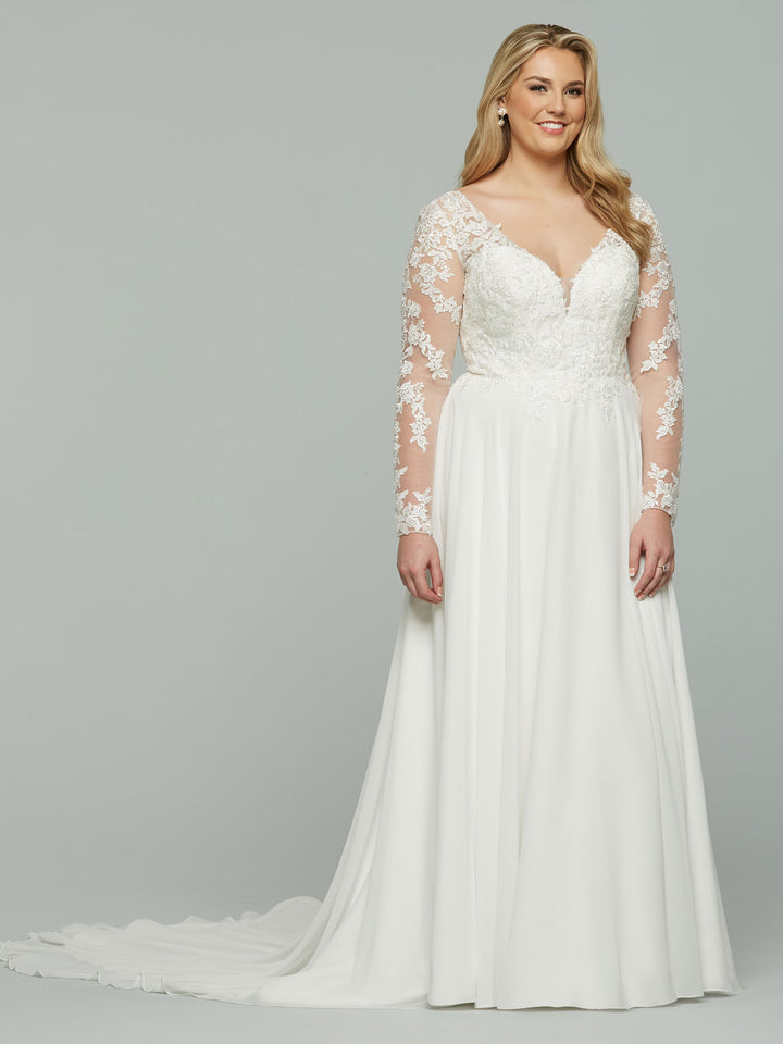 A woman in the Avery Austin "Francesca" gown—an ivory chiffon wedding dress with lace sleeves, lace bodice, and flowing train—stands smiling softly before a plain light gray background.